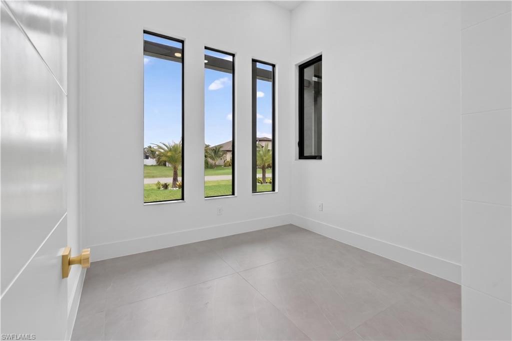 Room featuring three vertical windows with black frames, a smaller rectangular window with a black frame, light-toned tile flooring, and white walls