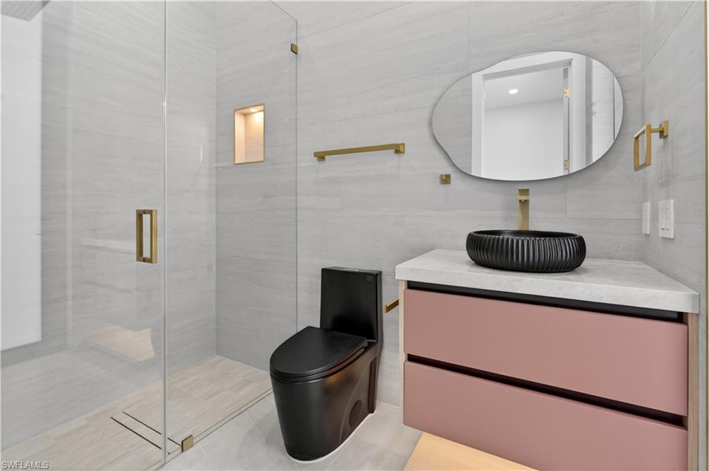Modern bathroom featuring a frameless glass shower enclosure, a black toilet, and a vanity with pink drawers