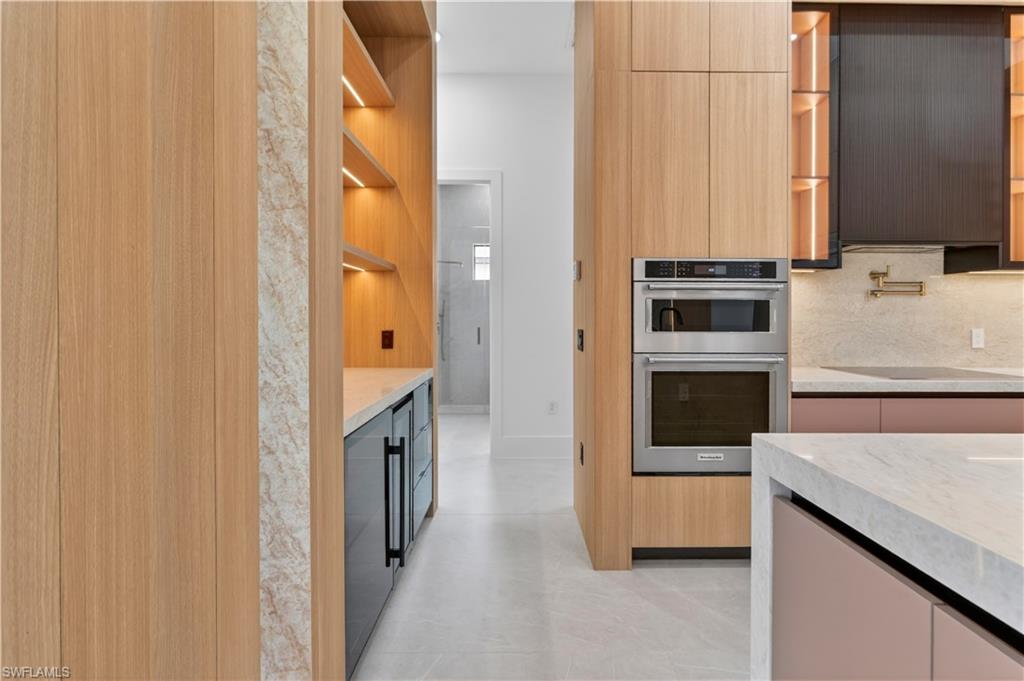 Kitchen featuring light wood-finish cabinetry, integrated stainless steel appliances, a built-in beverage cooler, and a light-toned countertop