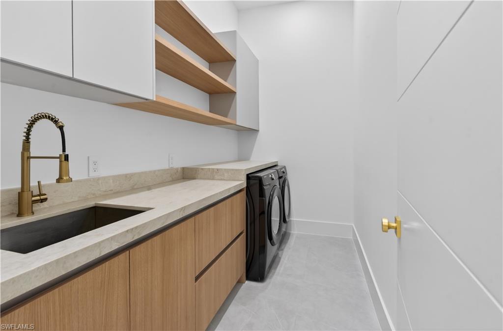 Laundry area featuring light wood-finish cabinetry, light-colored countertops, and a dark undermount sink with a brass-finish faucet
