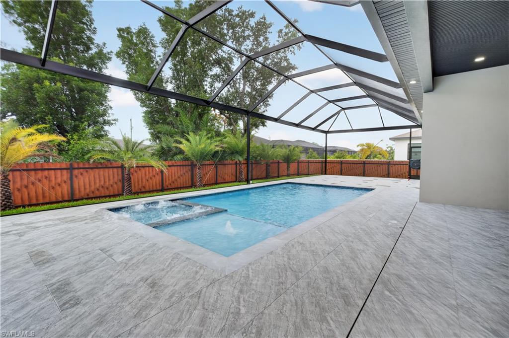 Screened-in outdoor living space featuring a rectangular pool with integrated spa and water feature, expansive gray-toned tile patio, and a privacy fence