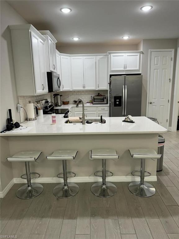 Kitchen with kitchen peninsula, appliances with stainless steel finishes, a kitchen bar, white cabinets, and light wood-type flooring