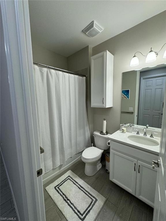 Full bathroom with wood-type flooring, vanity, shower / tub combo, and toilet