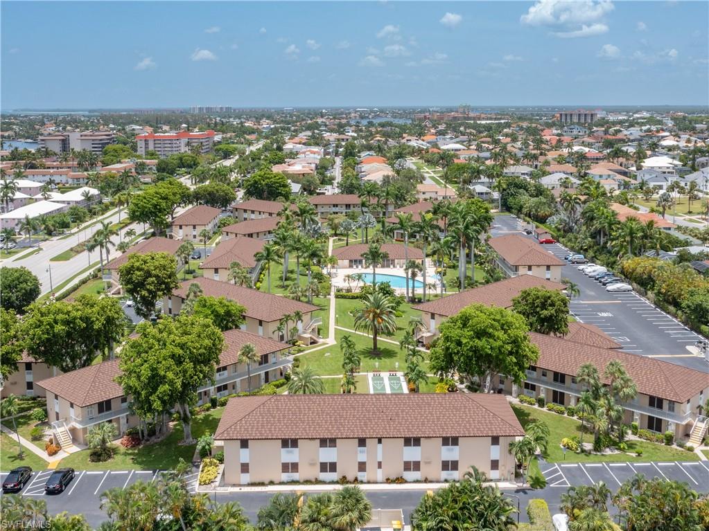Aerial perspective showcasing a multi-building residential complex featuring a central swimming pool, expansive paved parking areas, and mature palm tree landscaping