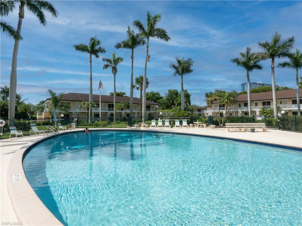Curved swimming pool featuring a light-colored coping, surrounded by a paved deck with lounge chairs and a wooden bench