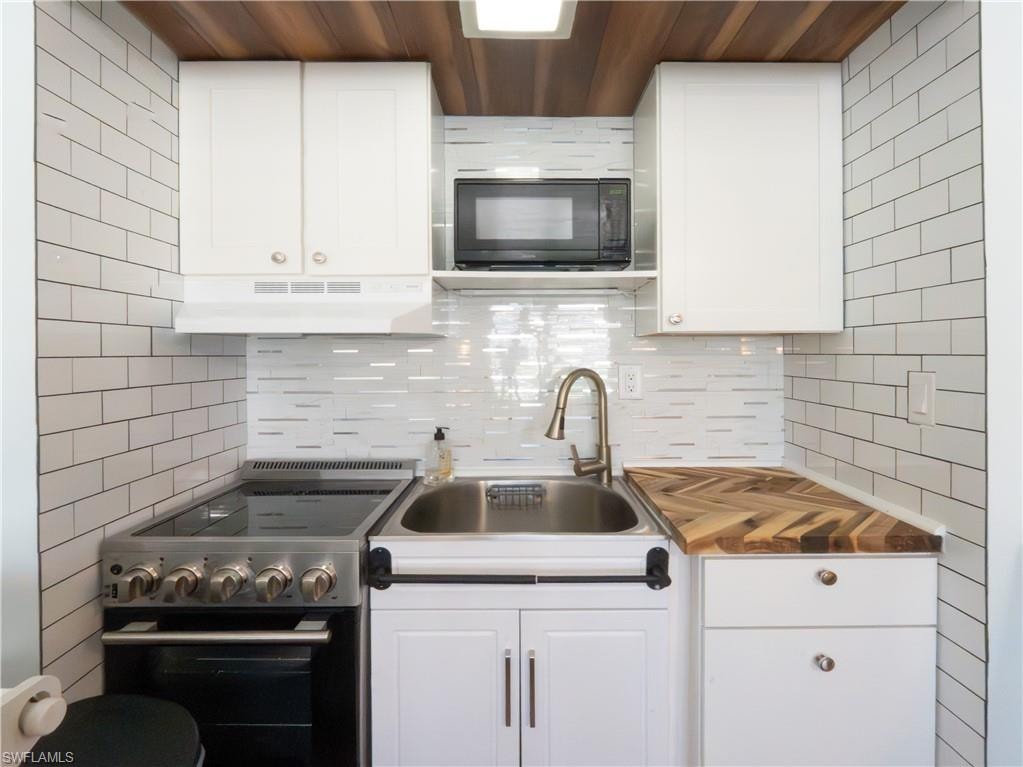 Compact kitchen featuring white shaker cabinetry, stainless steel sink with gooseneck faucet, a built-in microwave, and a herringbone wood-finish countertop