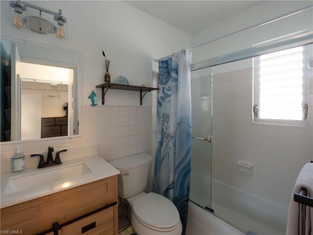 Bathroom featuring a wood-finish vanity with an integrated sink and matte black faucet, a bathtub with a glass shower enclosure, white subway tile surround, and a window with horizontal blinds