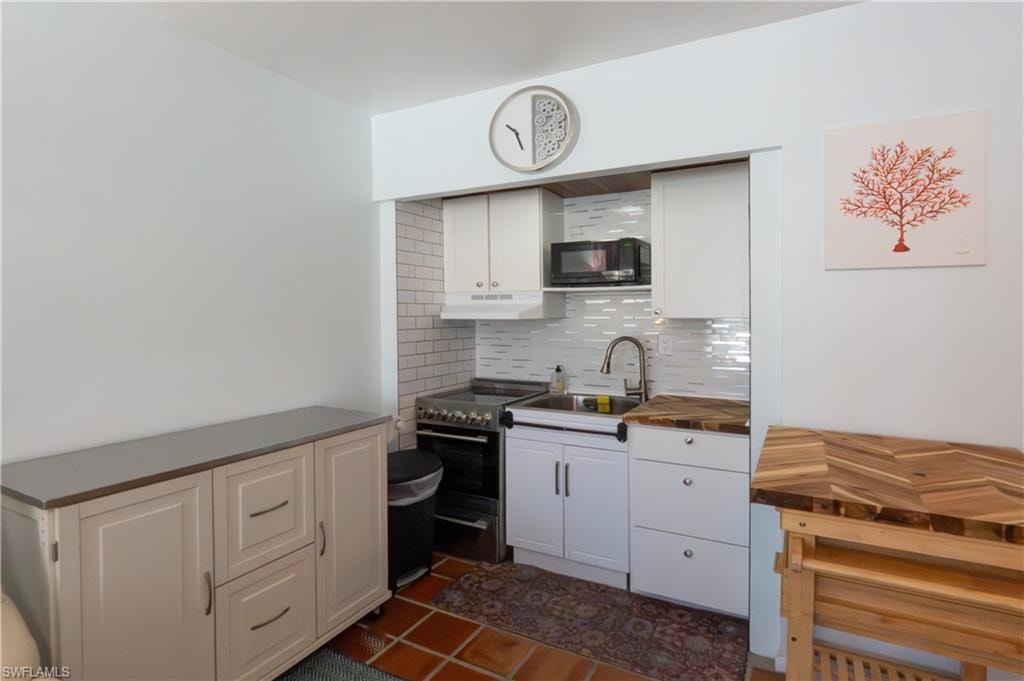 Compact kitchen area featuring white cabinetry, a subway tile backsplash, and a stainless steel sink with a gooseneck faucet