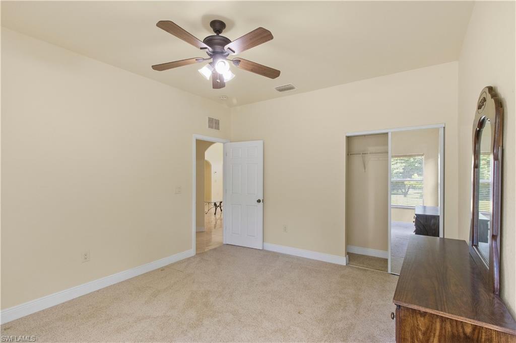 Carpeted room with vaulted ceiling and a wood-finish ceiling fan with integrated lighting