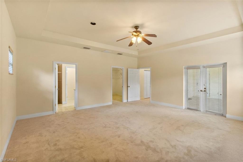 Spacious room featuring neutral carpeting and a tray ceiling with a built-in ceiling fan