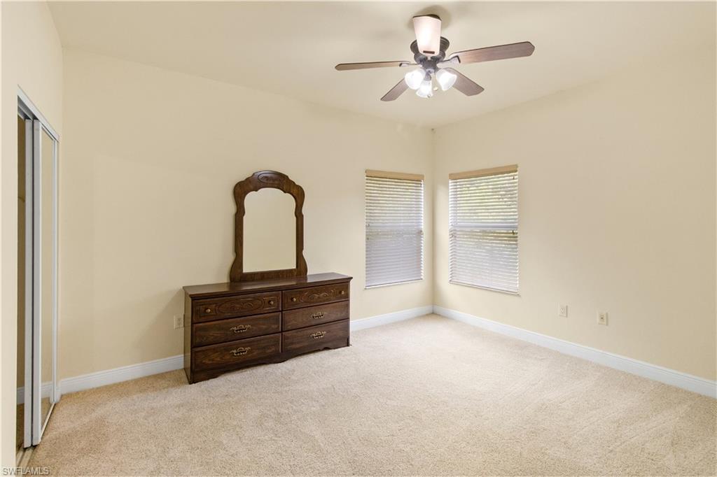 Bedroom featuring light beige carpeting, two windows with horizontal blinds, a ceiling fan with integrated lighting, and a closet with mirrored sliding doors