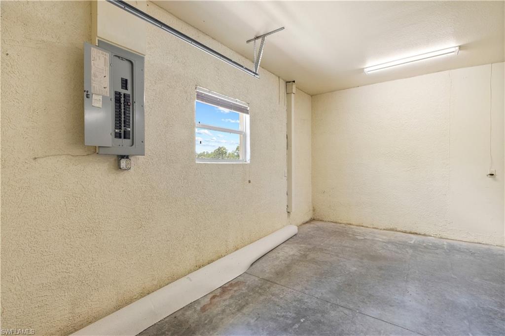 Utility space featuring concrete flooring, textured walls, a single window, and overhead fluorescent lighting