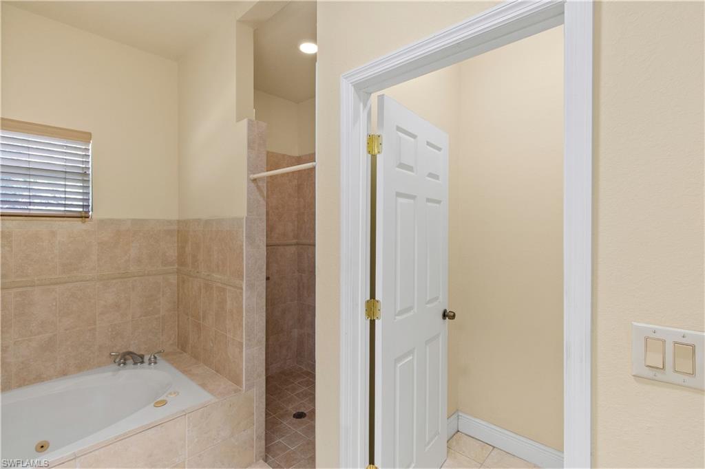 Spacious bathroom featuring a built-in jetted tub, tiled surround, and separate standing shower with tiled walls and floor