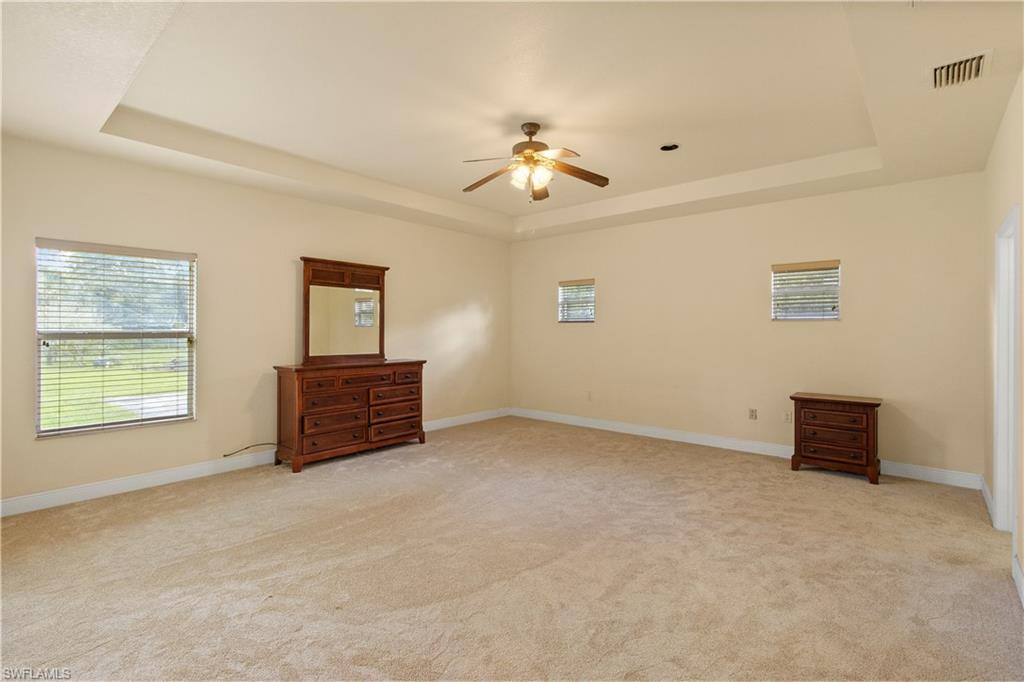 Spacious room featuring a tray ceiling with a ceiling fan, neutral carpeting, and multiple windows with blinds