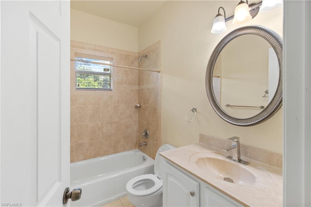 Bathroom featuring a white vanity with an integrated sink, a rectangular window with blinds, and a shower-tub combination with tiled walls
