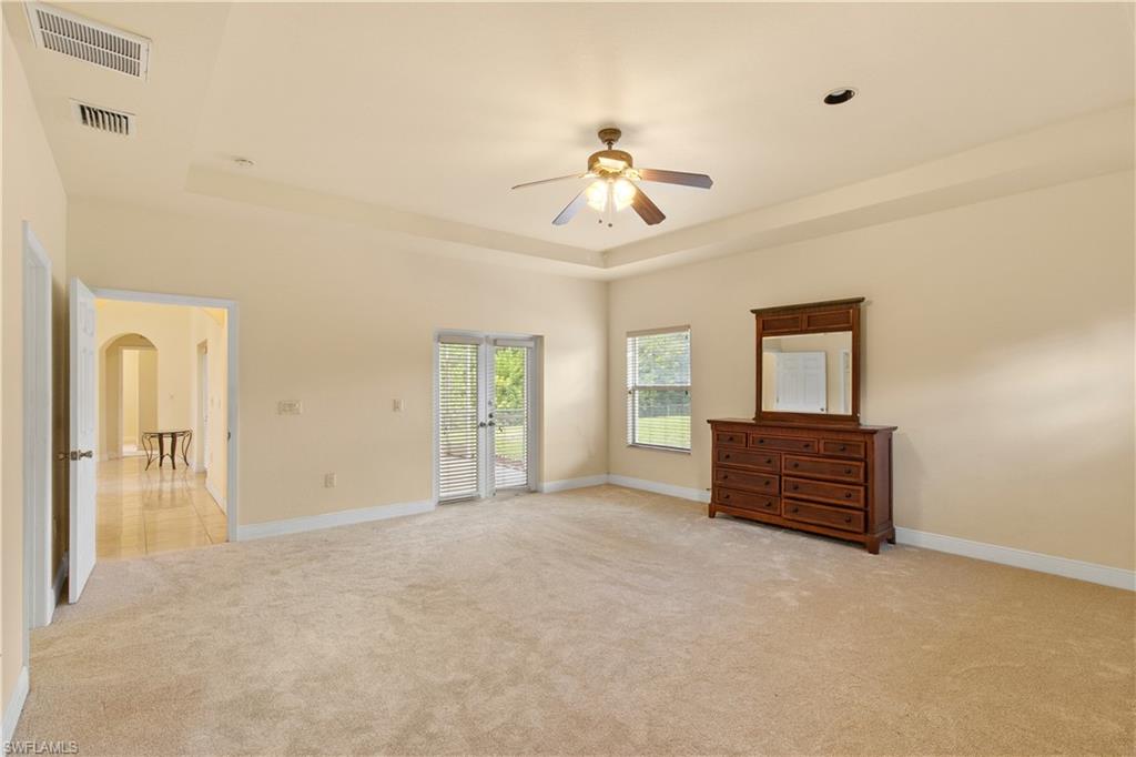 Spacious room featuring carpeting, tray ceiling with a ceiling fan, double French doors, and an arched doorway leading to a tiled hallway