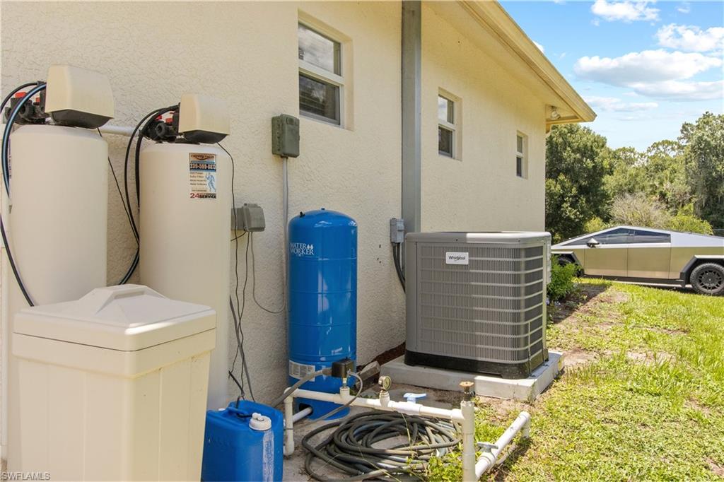 Exterior utility systems featuring a water treatment system with two large tanks, a blue pressure tank, and a modern air conditioning unit