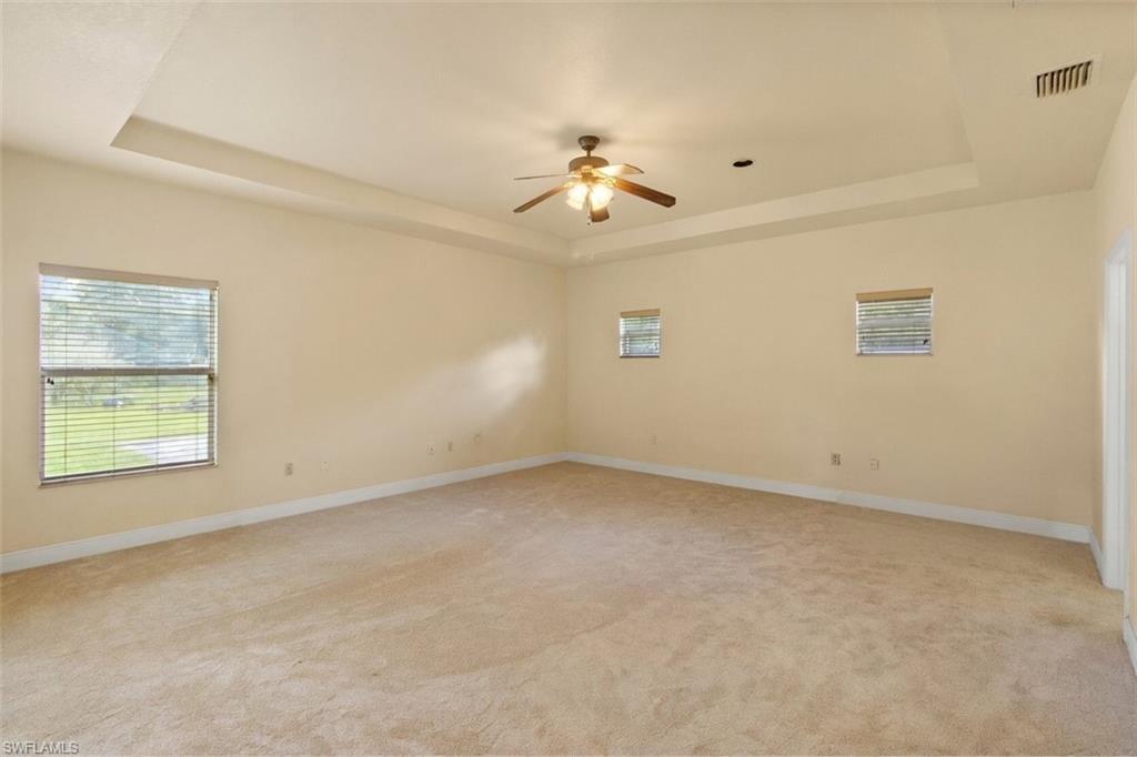 Expansive carpeted room featuring a tray ceiling, ceiling fan with integrated lighting, two windows with blinds, and recessed lighting