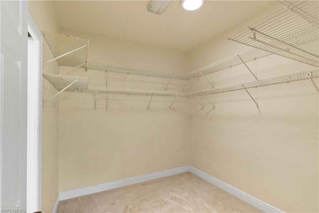 Walk-in closet featuring light beige walls, cream carpet flooring, white baseboards, and comprehensive wire shelving system