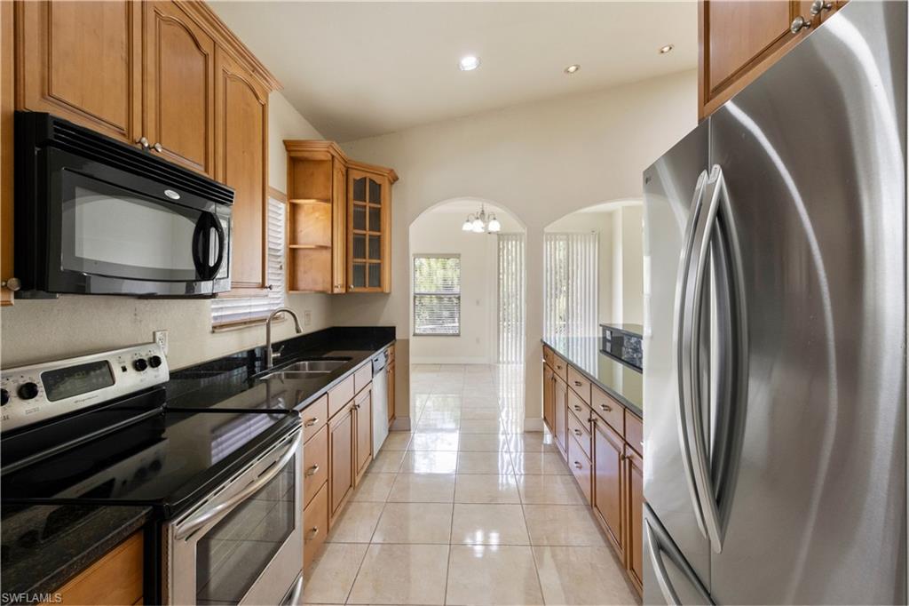 Kitchen featuring wood cabinetry, black countertops, stainless steel appliances, and tile flooring