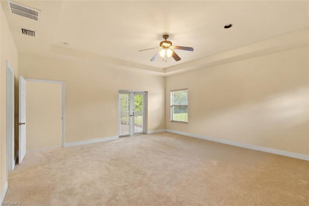 Spacious room featuring tray ceiling, ceiling fan, neutral carpet flooring, double French doors with blinds, and a single window