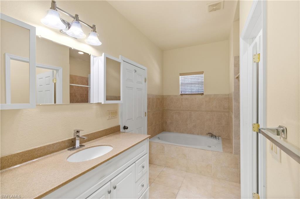 Bathroom featuring a built-in bathtub, tile surround, and a vanity with a light-toned countertop