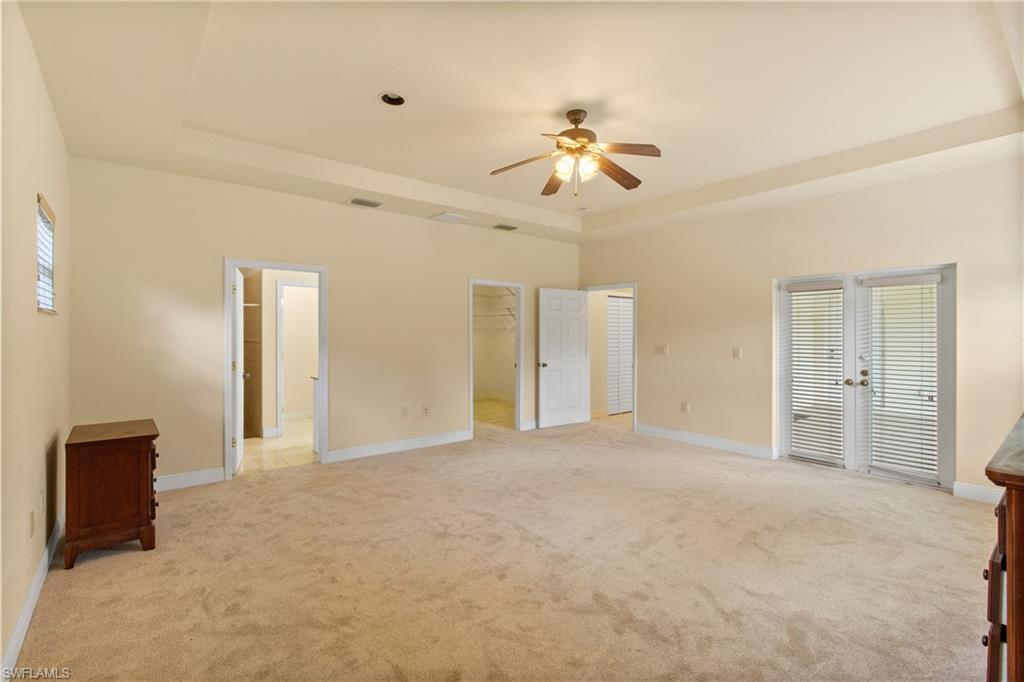 Spacious room featuring neutral carpeting, a tray ceiling with a ceiling fan, and double French doors with integrated blinds