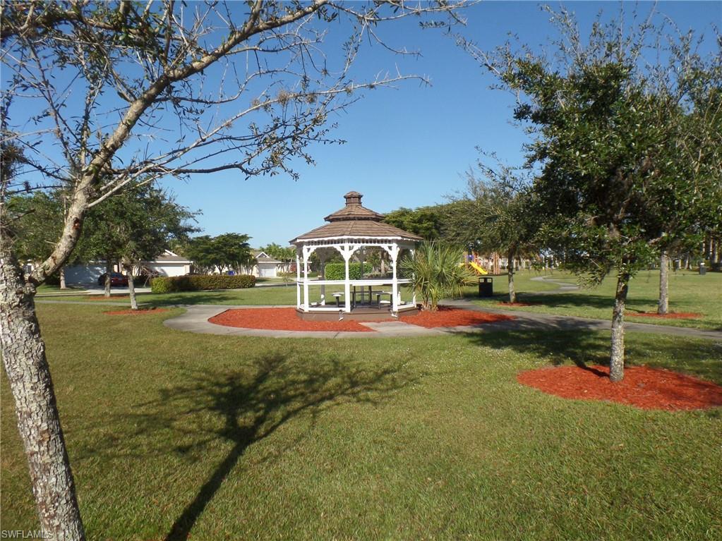 Expansive green space featuring a white gazebo with a brown shingled roof, manicured lawns, mature trees, and red mulch landscaping