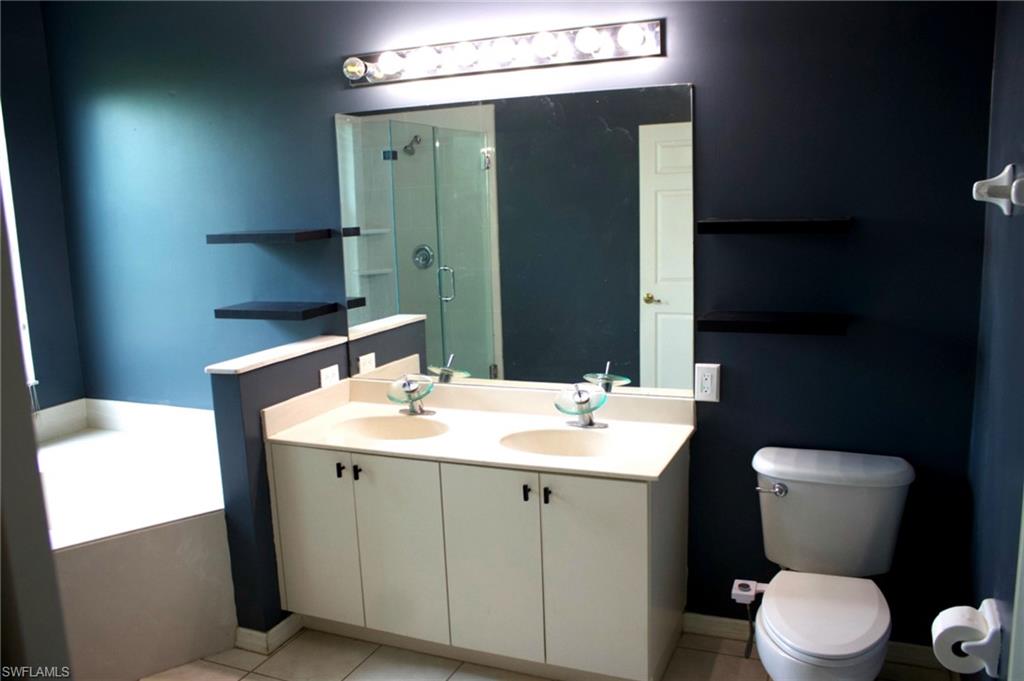 Bathroom featuring a dual vanity with vessel sinks, a glass-enclosed shower, a built-in soaking tub, and wall-mounted shelving