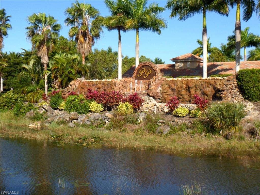 Prominent stone-faced entry monument with a water feature, lush tropical landscaping, and mature palm trees