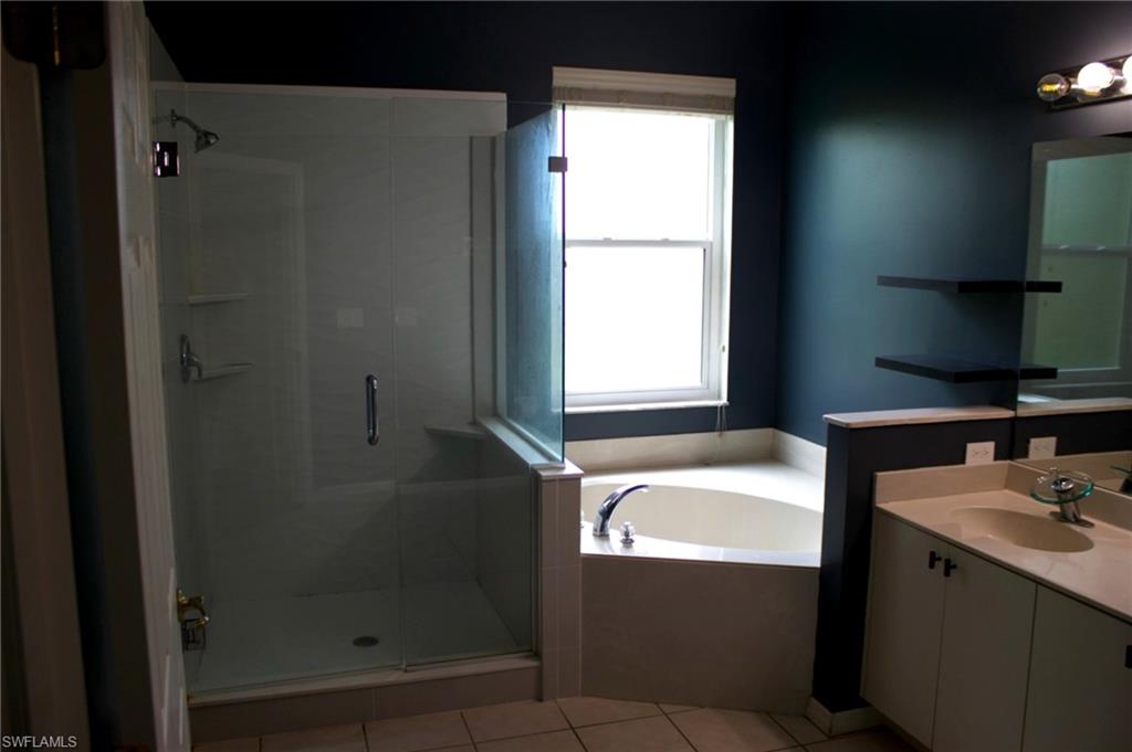 Bathroom featuring a glass-enclosed shower, a built-in corner soaking tub, a double vanity with an integrated countertop, and a window