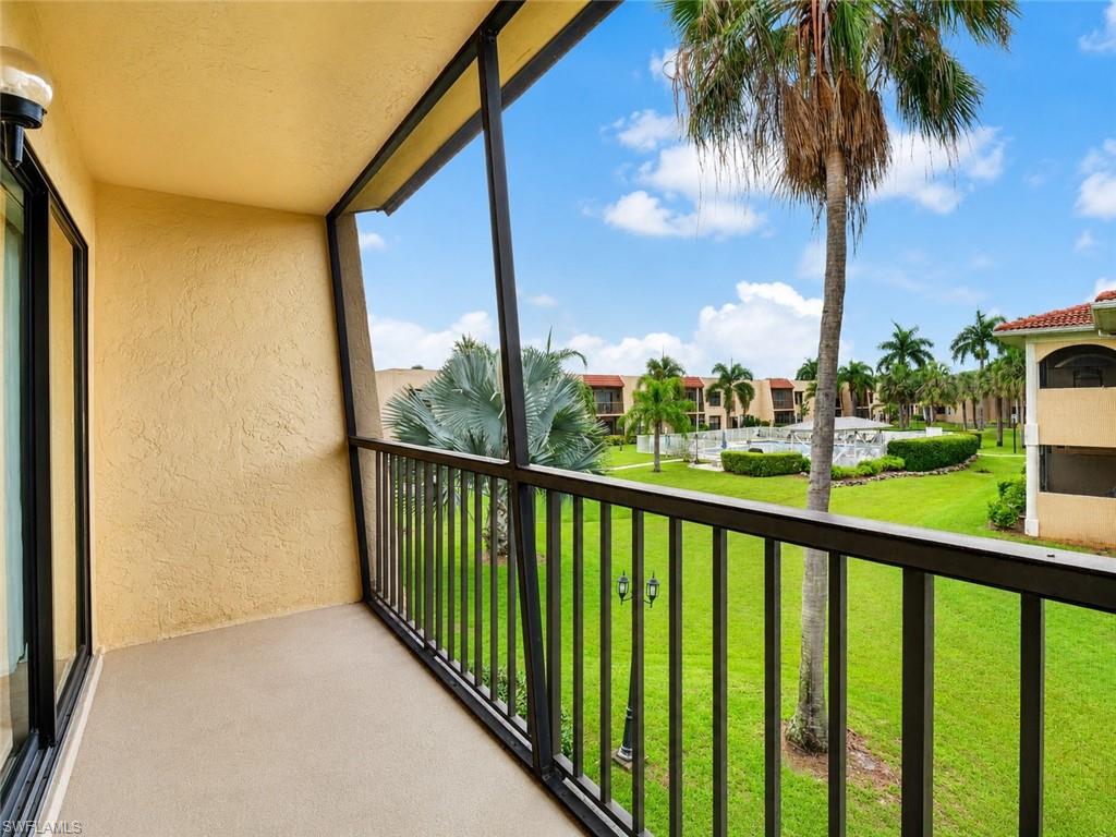 Screened balcony overlooking a landscaped common area with mature palm trees, a swimming pool, and multiple residential buildings