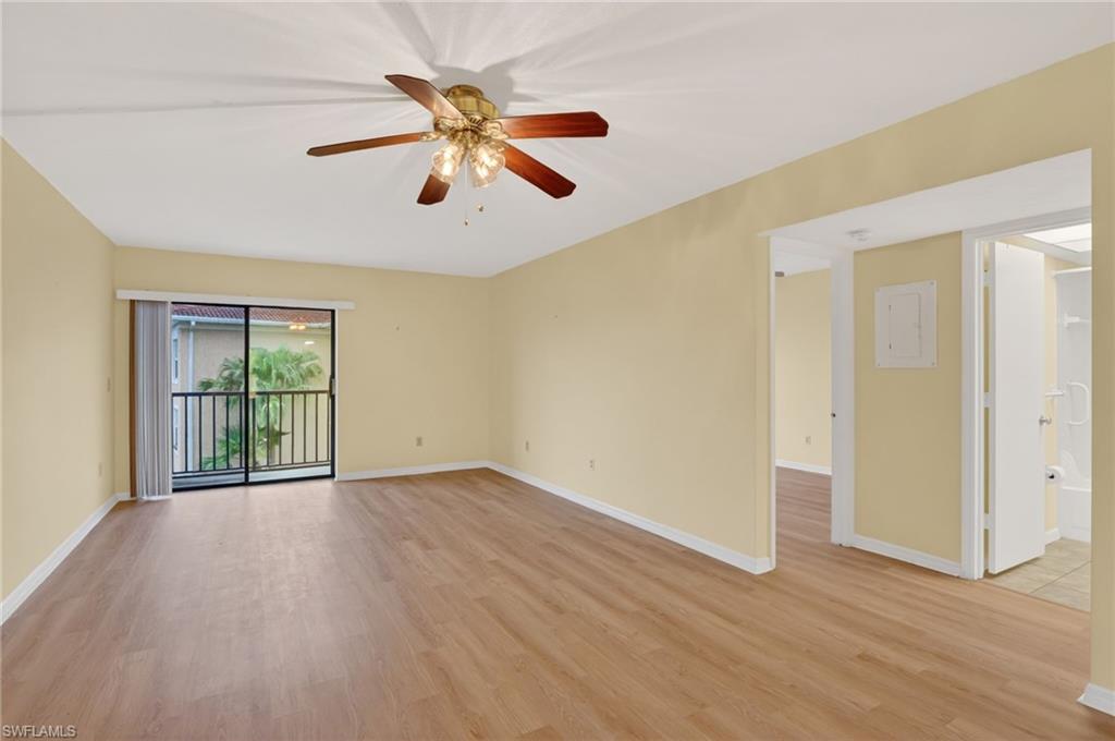 Spacious interior featuring wood-finish flooring, a ceiling fan with integrated lighting, and a sliding glass door opening to a balcony with black metal railings