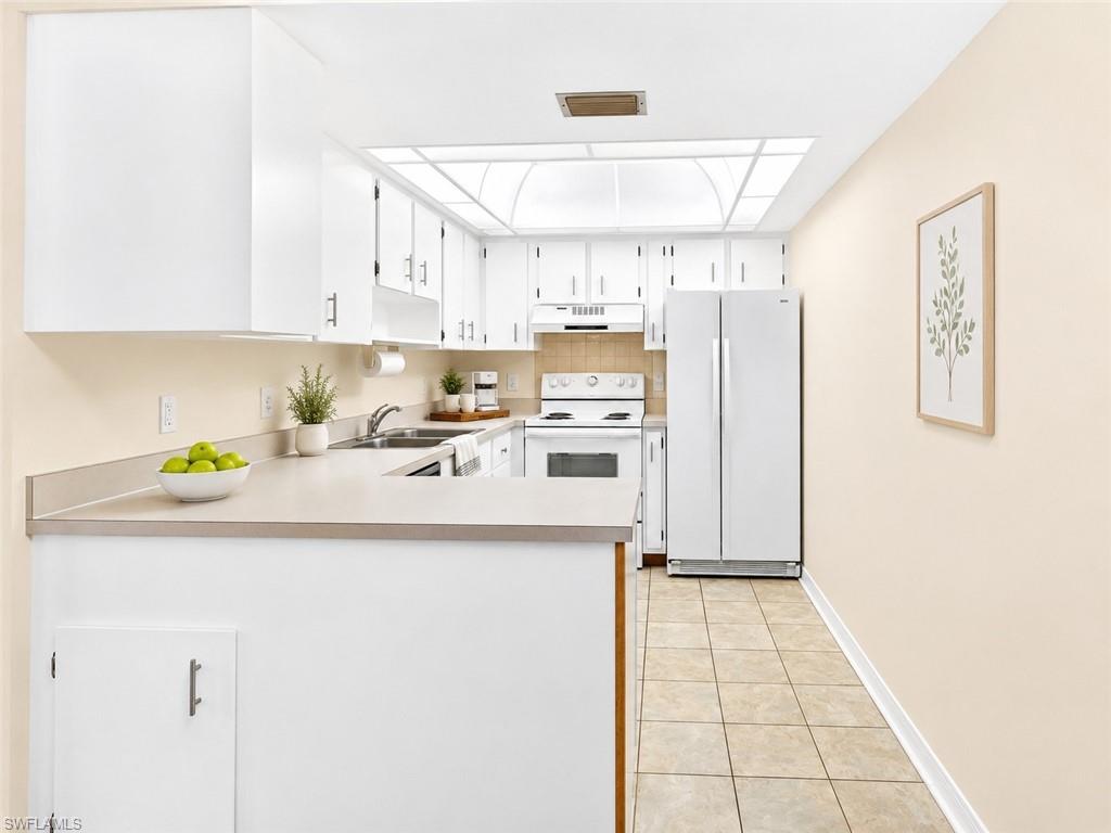 Kitchen featuring white cabinetry, light-toned countertops, a dual-basin sink, and tile flooring