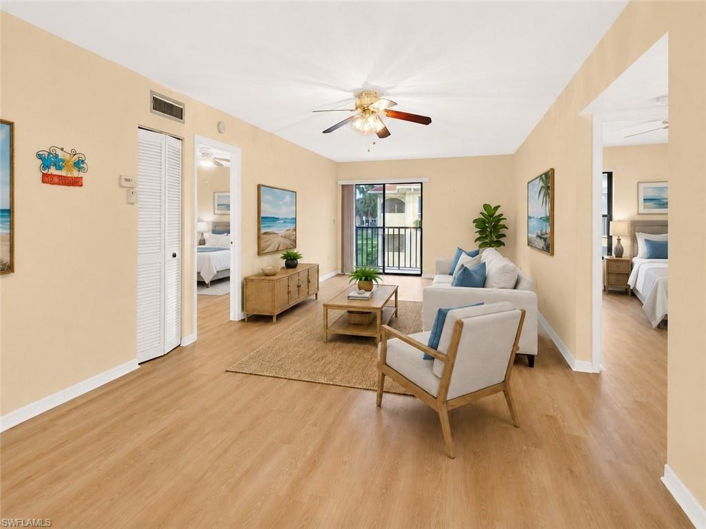 Spacious living area featuring wood-finish flooring, light-toned walls, a ceiling fan, and a balcony