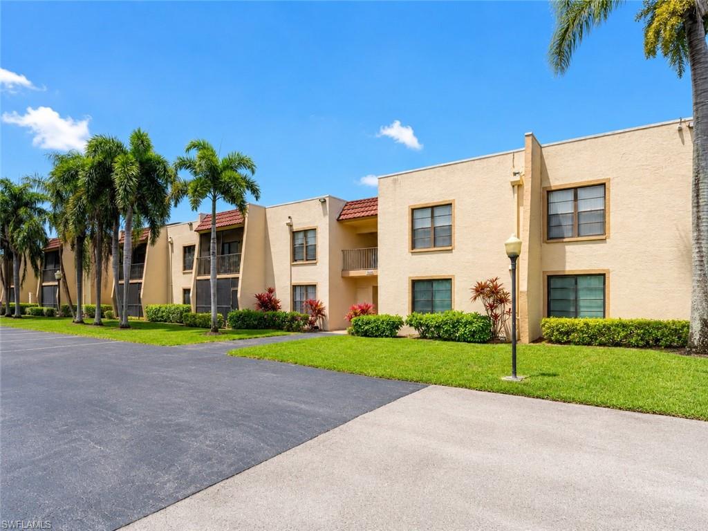 Multi-story stucco building featuring tiled roofing, private screened balconies, and well-maintained landscaping