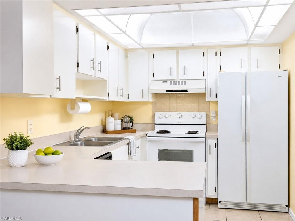 Kitchen featuring white cabinetry, light countertops, a double basin stainless steel sink, and white appliances