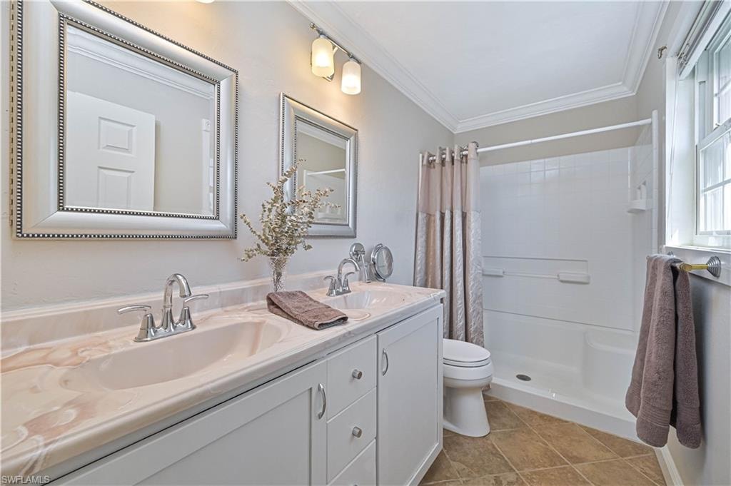 Dual vanity with integrated sinks, framed mirrors, chrome fixtures, crown molding, and tiled flooring