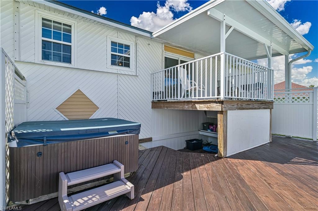 Expansive wood-finish deck with a built-in hot tub, covered balcony featuring white railings, and white lattice fencing
