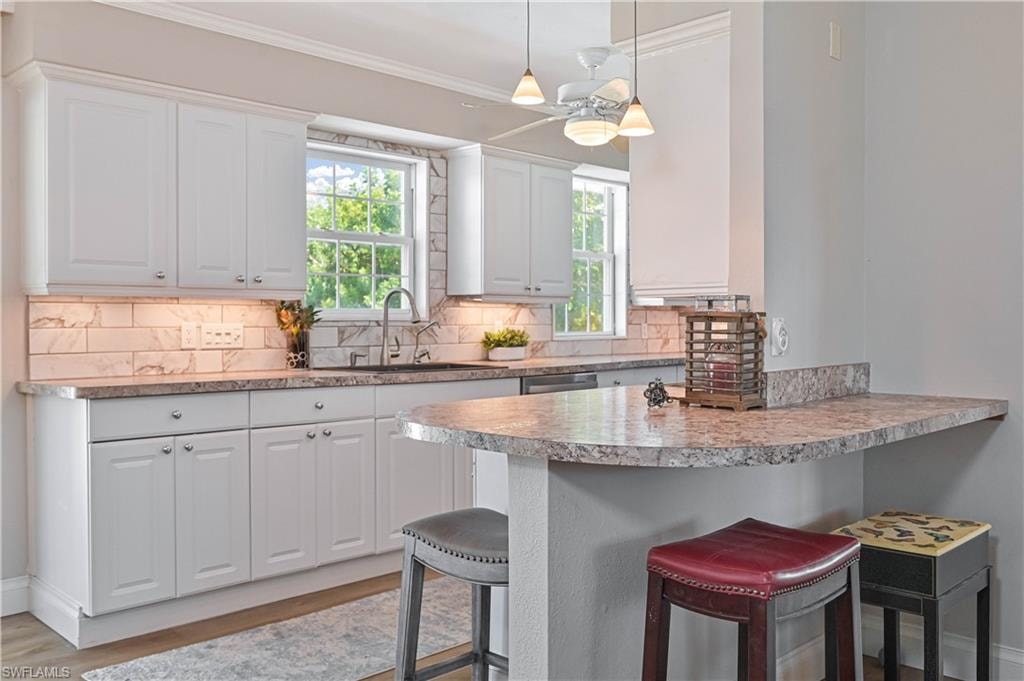 White cabinetry, light-toned countertops, tile backsplash, stainless steel sink, and a breakfast bar