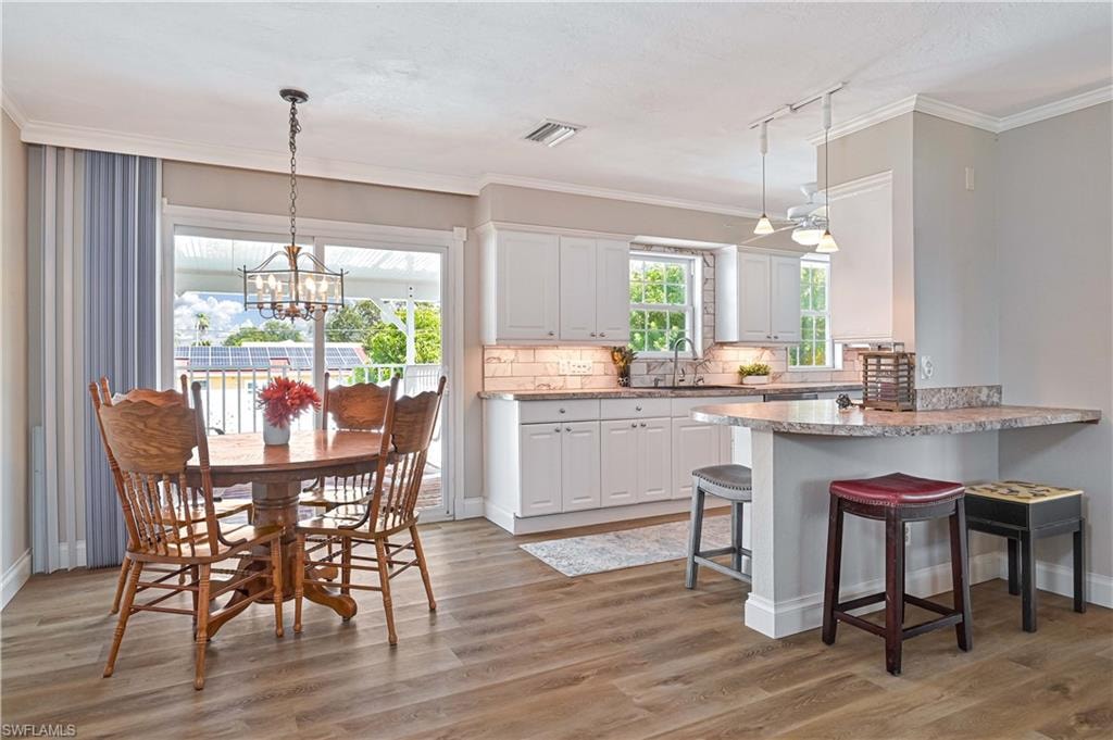 Wood-finish flooring, white cabinetry, a built-in breakfast bar, pendant lighting, and a glass sliding door