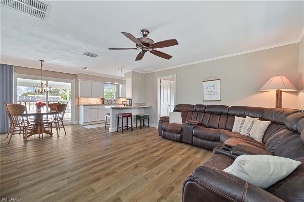Open-concept living area with wood-finish flooring, a ceiling fan, and crown molding