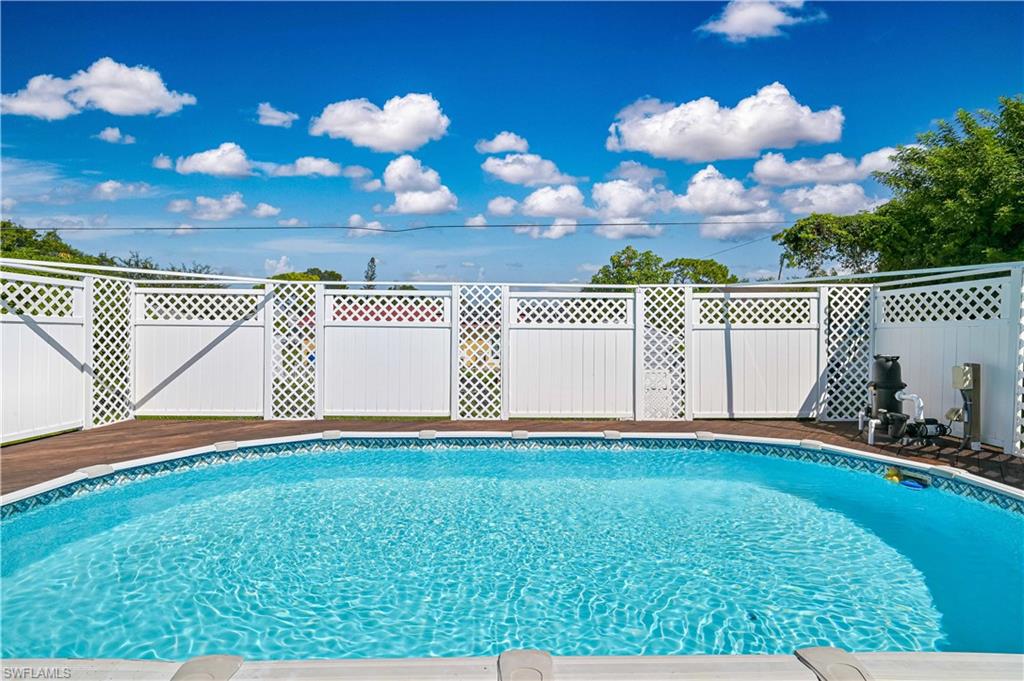 In-ground swimming pool with a wood-finish deck surround, complemented by a white lattice-top fence