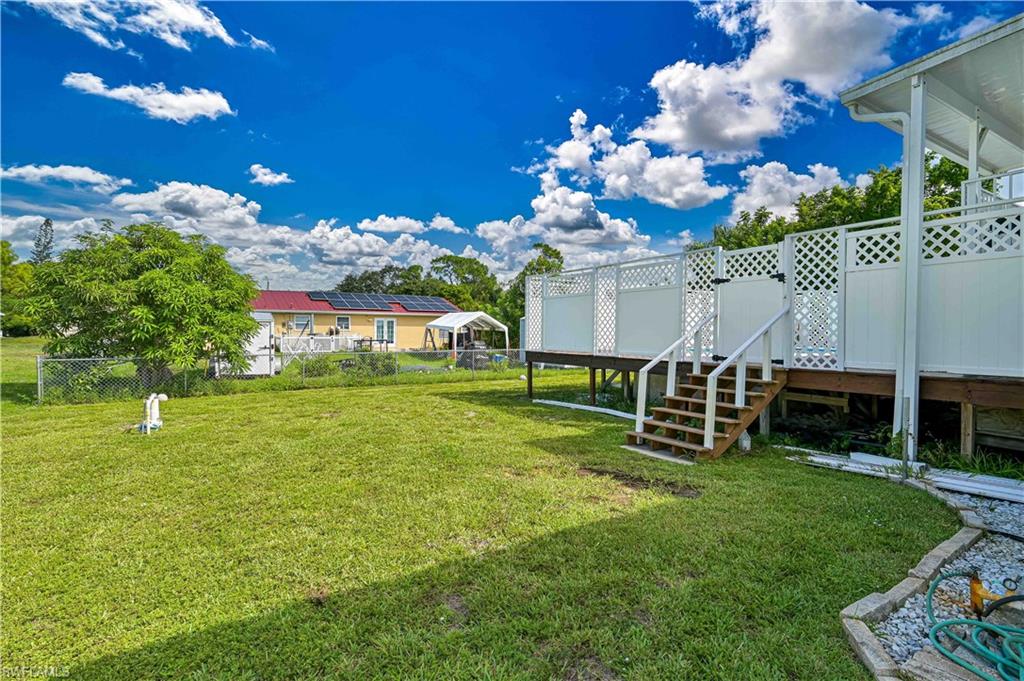 Expansive grassy yard with a raised deck featuring white lattice privacy screens and wooden steps