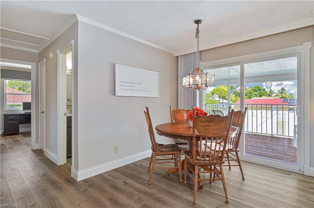 Dining area with warm wood-finish flooring, round wood dining table, and French doors opening to a covered deck with metal railing