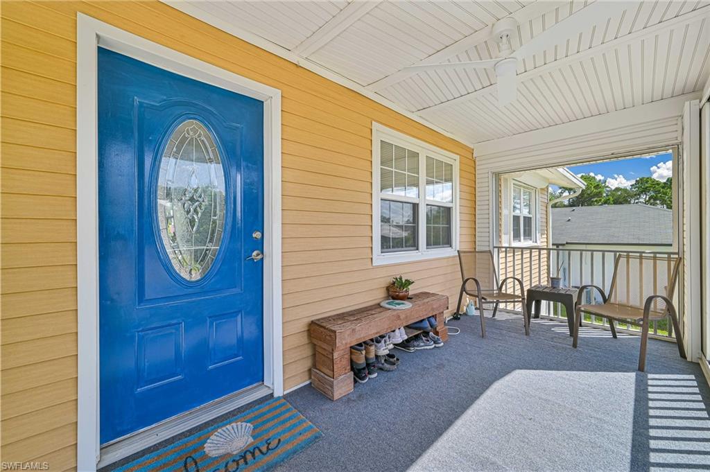 Screened porch with light tan siding, a bright blue entry door featuring an oval decorative glass insert, and a white ceiling fan