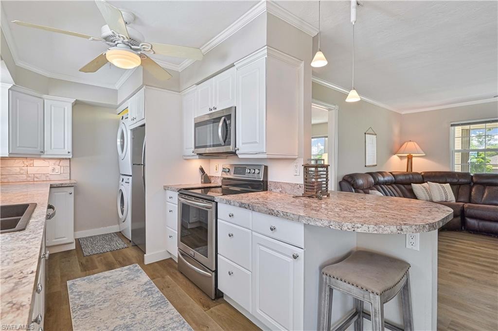 White cabinetry with stainless steel appliances, stone-finish countertops, tile backsplash, and wood-finish flooring
