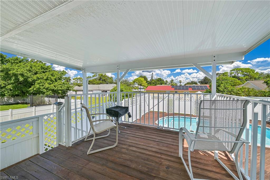 Covered outdoor deck with wood-finish flooring, white railing, and a swimming pool