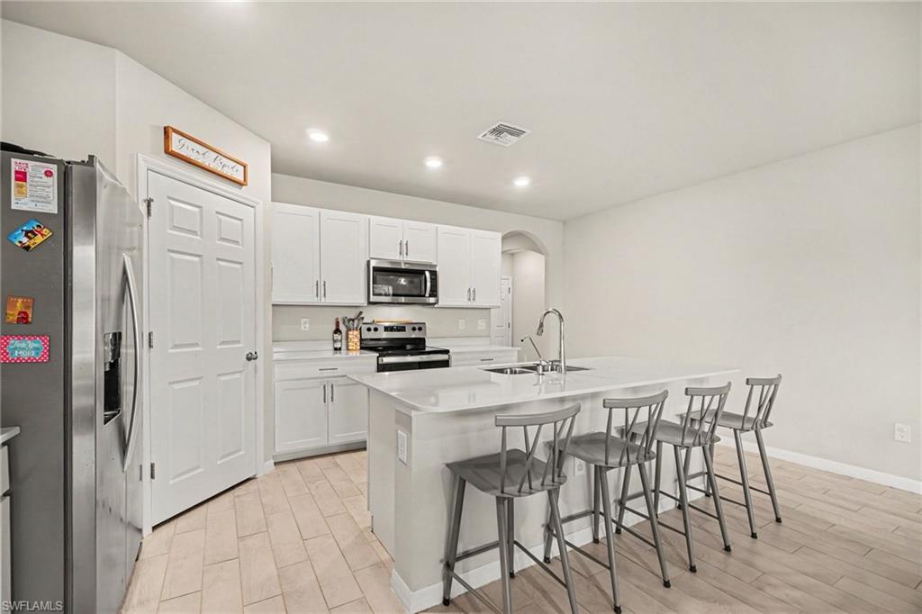 Modern kitchen featuring white cabinetry, a large center island with seating, stainless steel appliances, and light wood-finish flooring