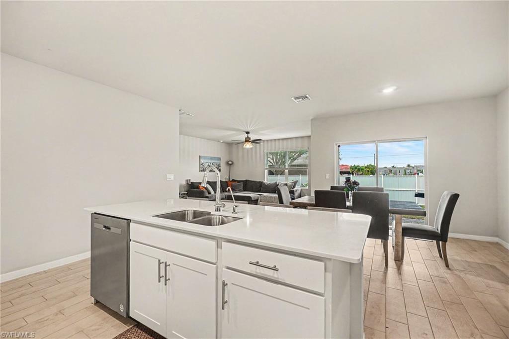 Central kitchen island featuring a double-basin stainless steel sink with a high-arc faucet, integrated dishwasher, and white cabinetry
